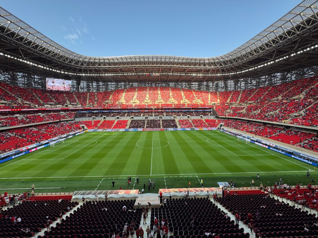 A vibrant football stadium with a broad green field and red seats filled with sports fans.